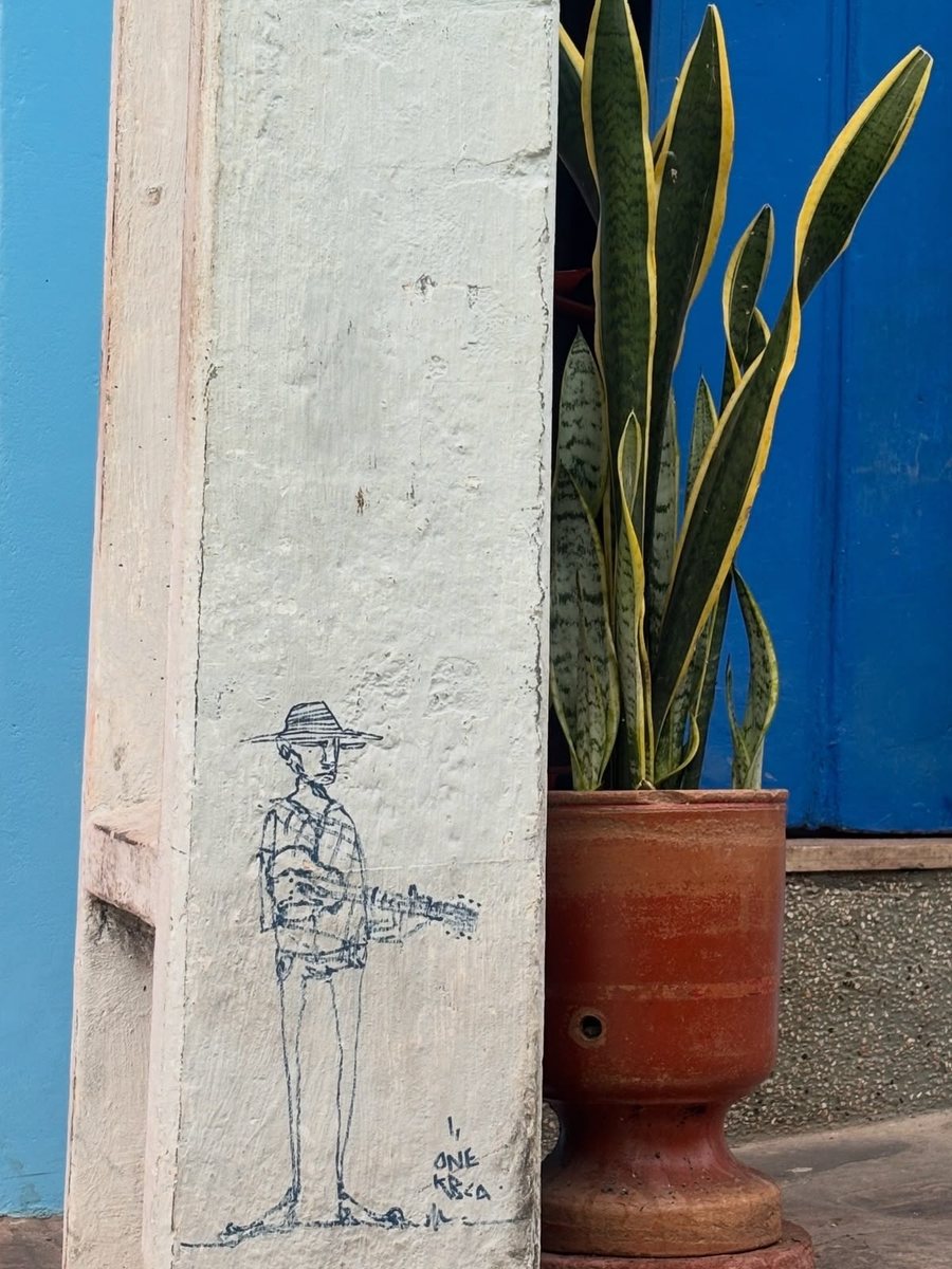 Desenho de uma figura com chapéu junto a uma porta azul e uma planta.