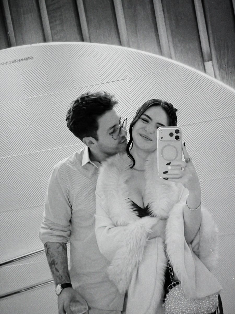 Duas pessoas diante de um espelho, em uma fotografia em preto e branco.